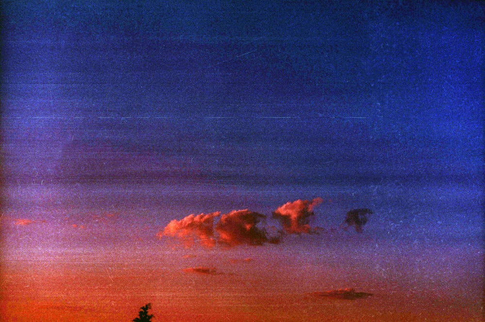 a red and blue sky with clouds and trees