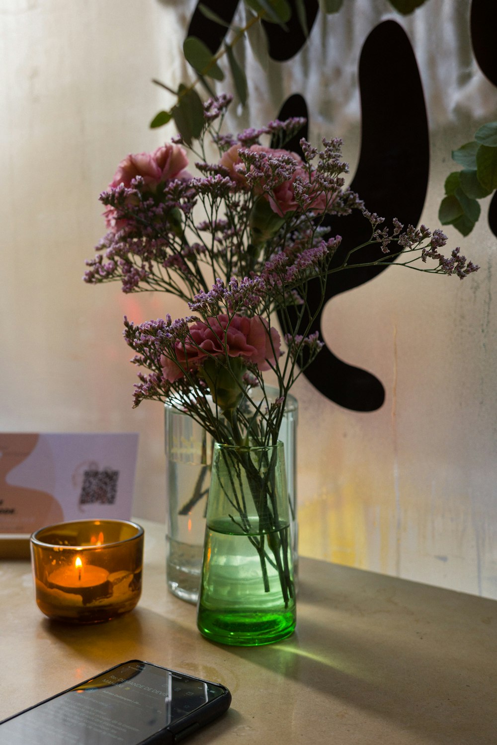 a vase of flowers sitting on a table next to a cell phone