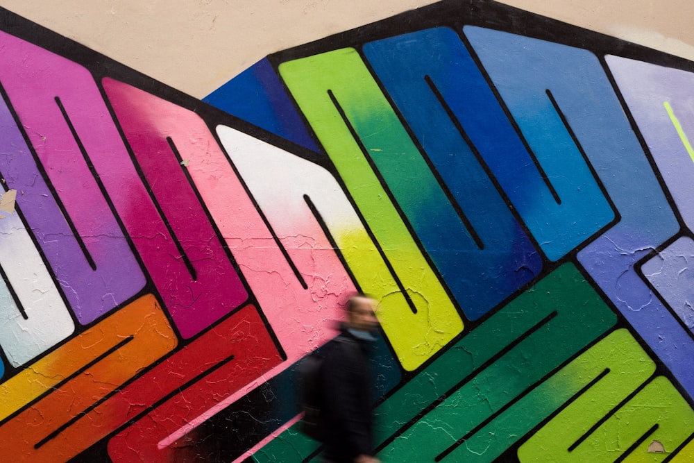 uma pessoa passando por uma parede com um mural colorido sobre ele