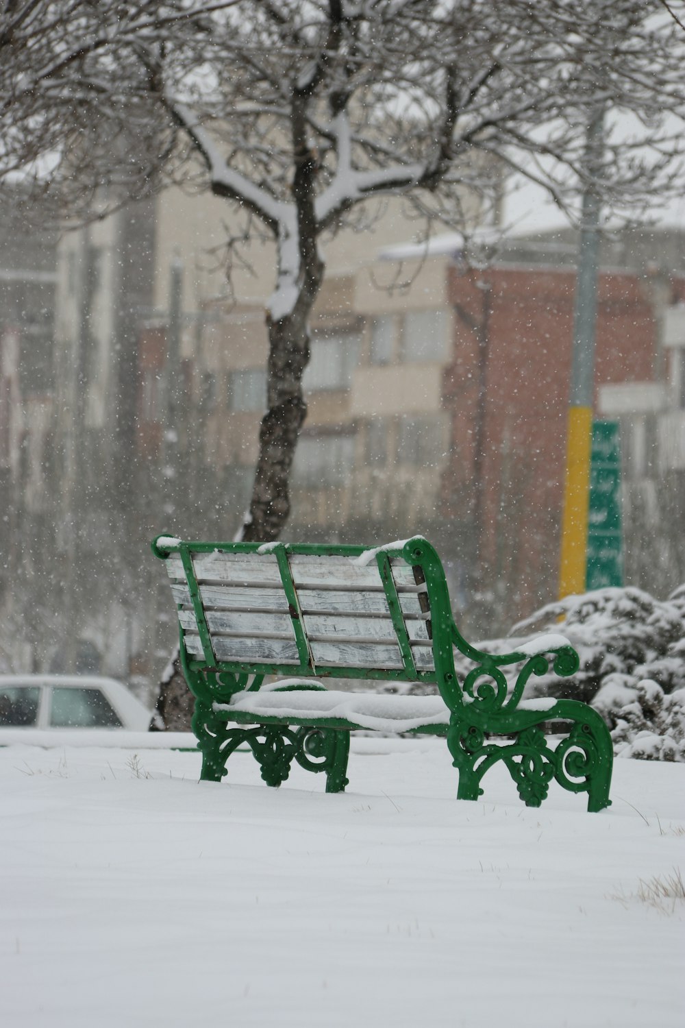 a park bench covered in snow next to a tree