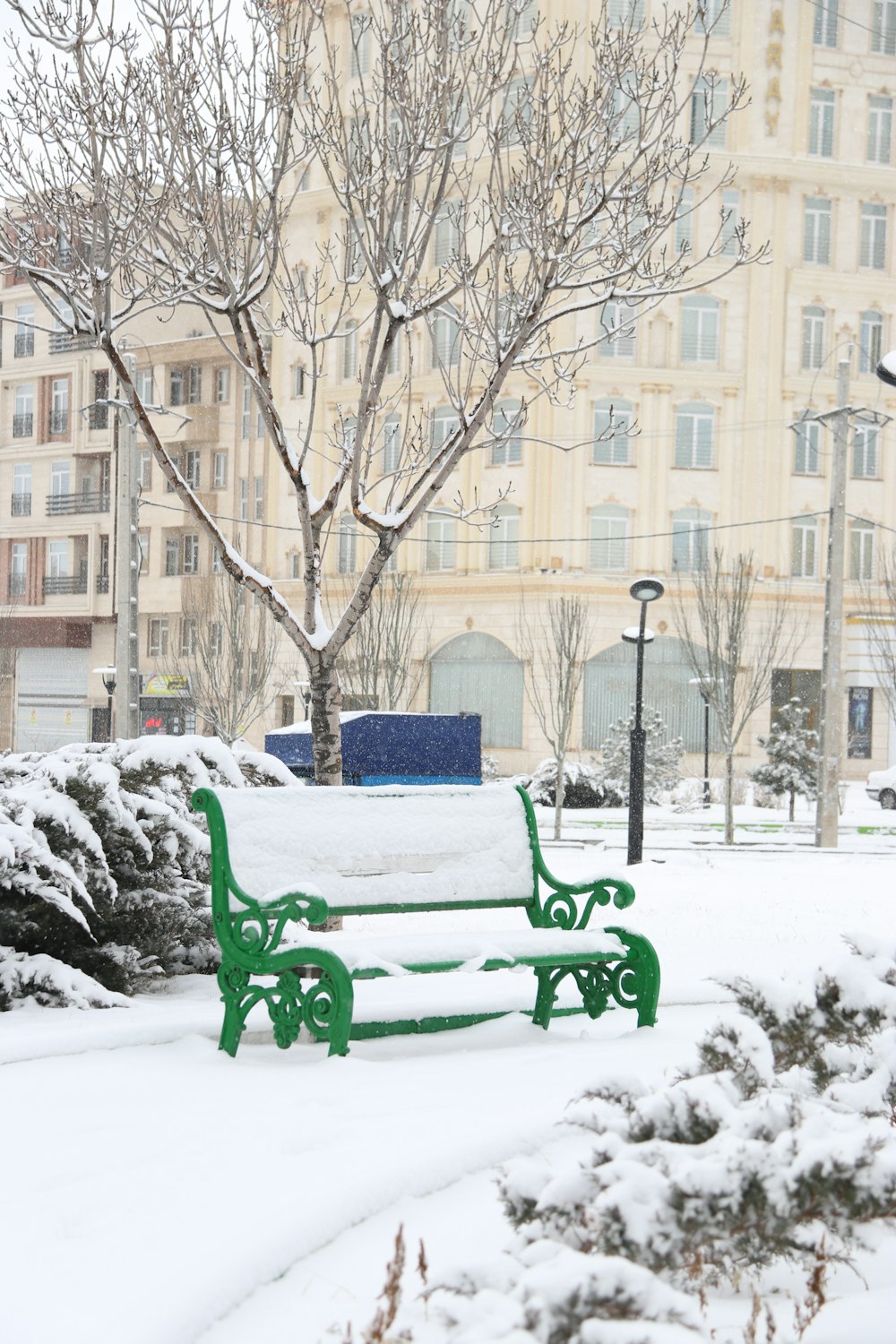 a green park bench covered in snow next to a tree