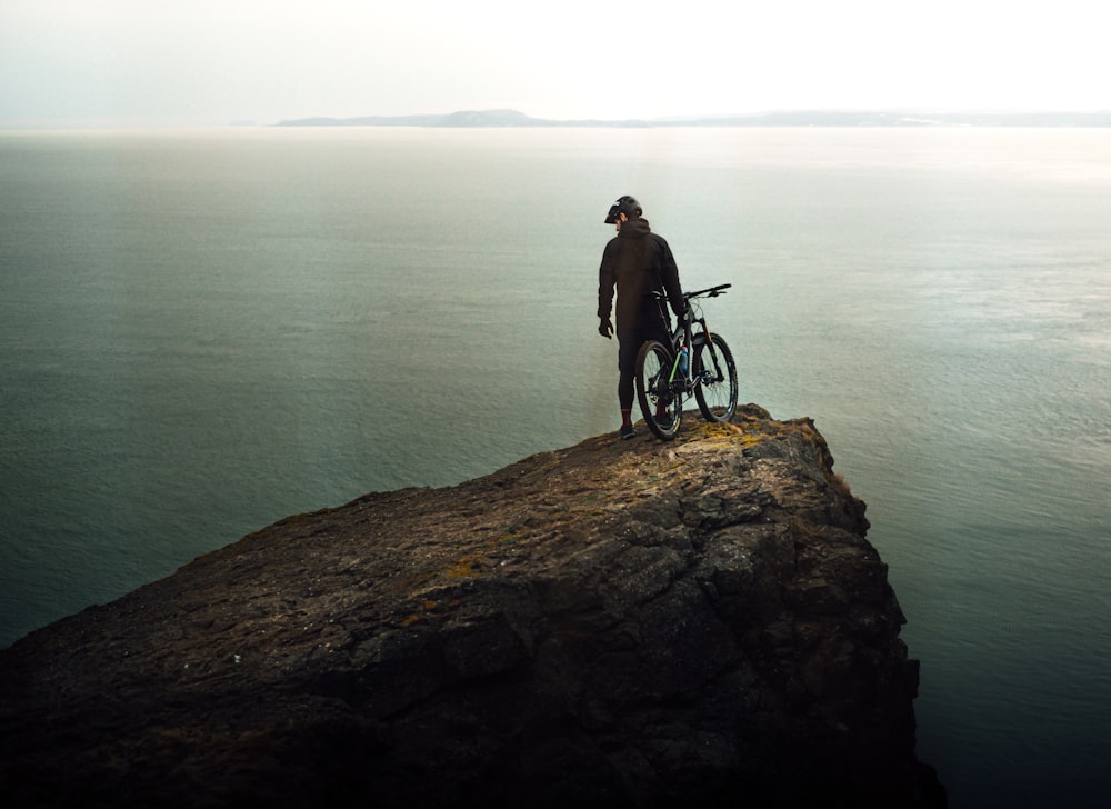 a man standing on top of a cliff next to a bike