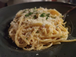 A rich, creamy pasta dish topped with fresh herbs and grated cheese in a cozy kitchen setting