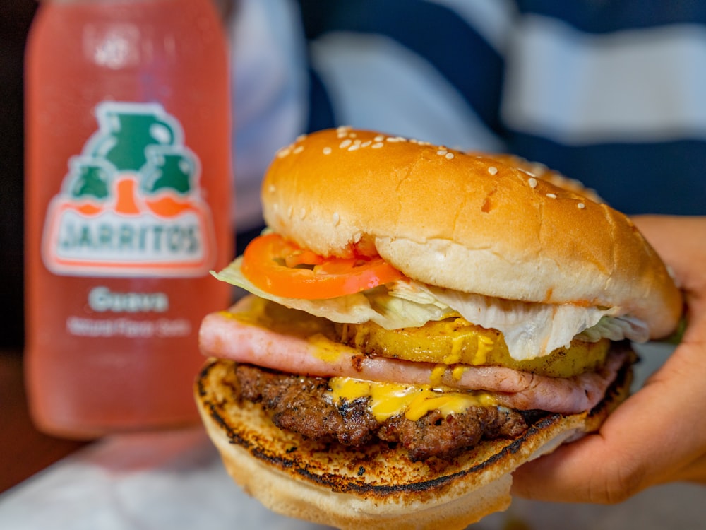 a person holding a hamburger and a bottle of juice