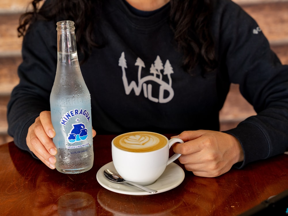 Una mujer sentada en una mesa con una taza de café y una botella de agua