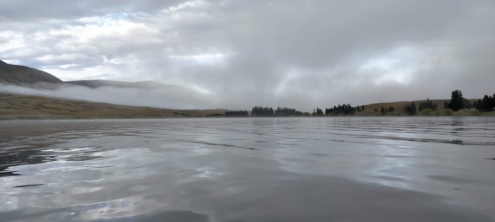 a body of water surrounded by mountains under a cloudy sky