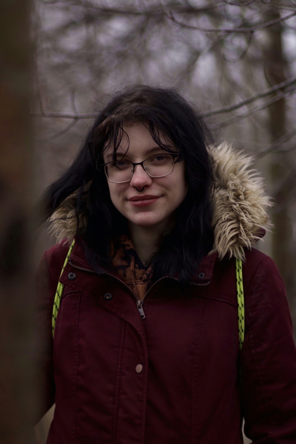 uma mulher vestindo óculos e uma jaqueta na floresta