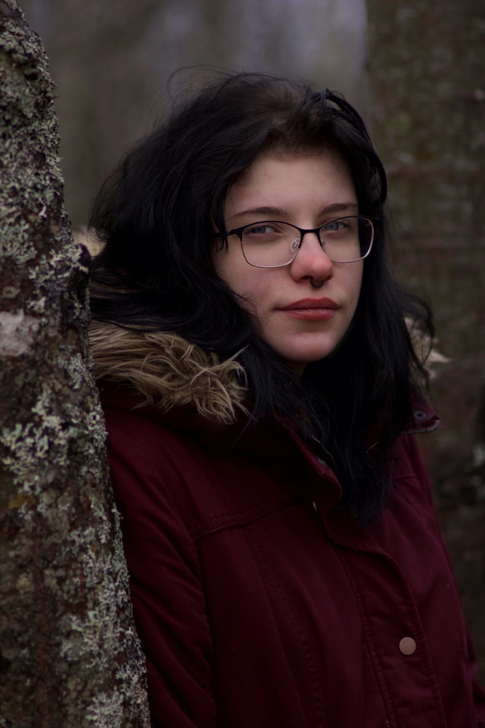 a woman wearing glasses standing next to a tree