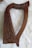 A wooden harp with intricate carved details on its frame is placed on a fluffy white surface. The harp has a curved shape with several strings, including one colored red and another blue.
