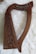 A wooden harp with intricate carved details on its frame is placed on a fluffy white surface. The harp has a curved shape with several strings, including one colored red and another blue.