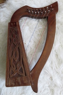 A wooden harp with intricate carved details on its frame is placed on a fluffy white surface. The harp has a curved shape with several strings, including one colored red and another blue.