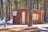 A small, rustic wooden cabin is situated in a forested area during winter. The cabin is adorned with various vintage license plates on its exterior. Snow covers the ground surrounding the cabin, while tall pine trees envelop the structure, casting shadows on the snow.