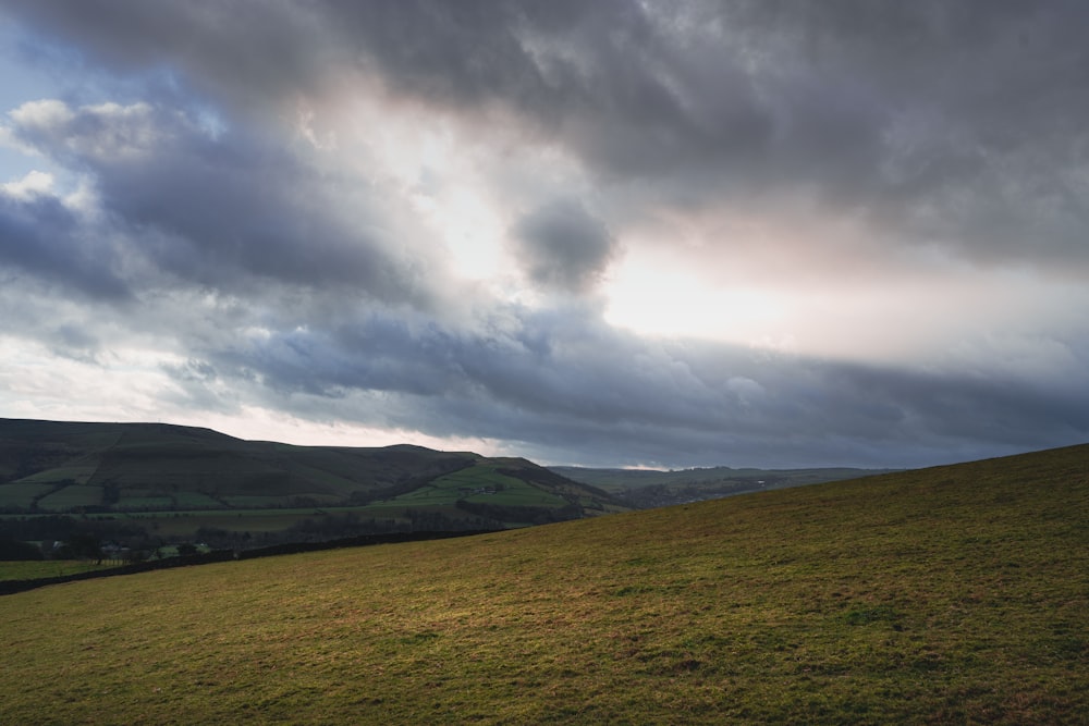 a grassy hill with a cloudy sky above it