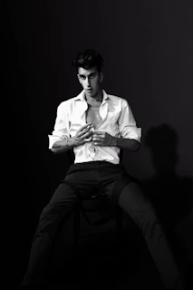 Editorial-style image featuring a model seated against a white backdrop wearing a crisp white shirt and black trousers with elegant serif typography overlay