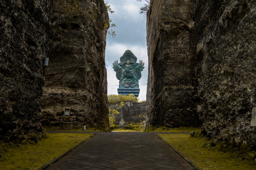 a stone walkway between two large rocks with a statue in the background