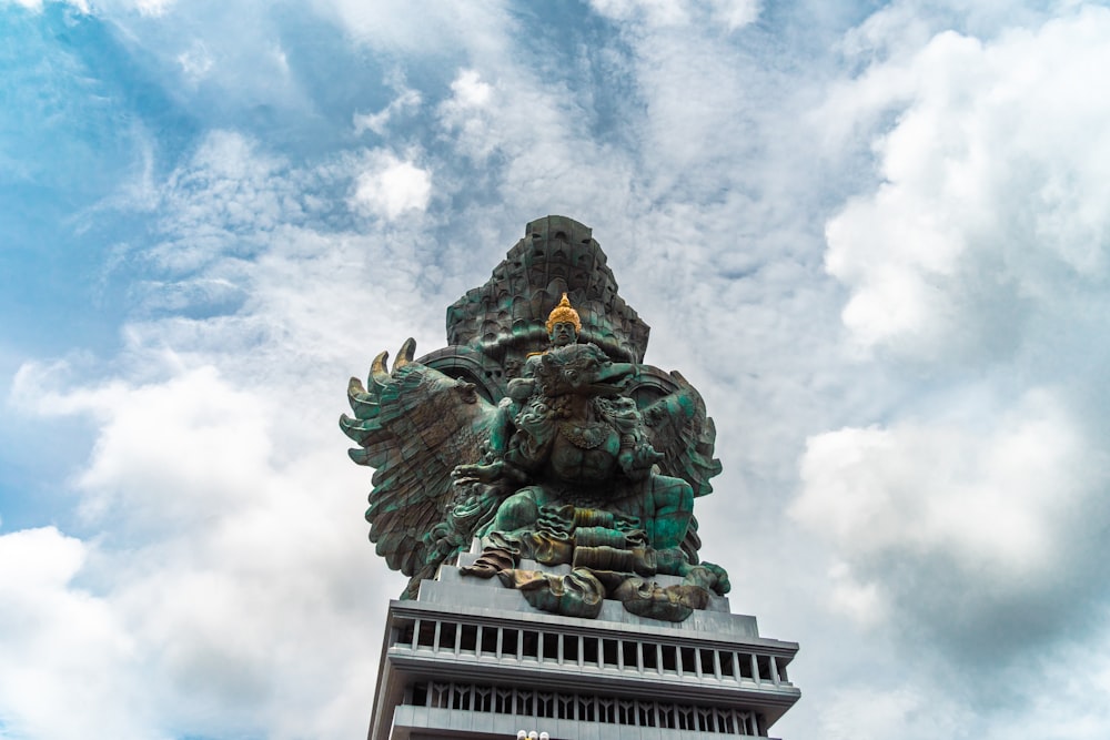 uma estátua no topo de um edifício com nuvens no fundo