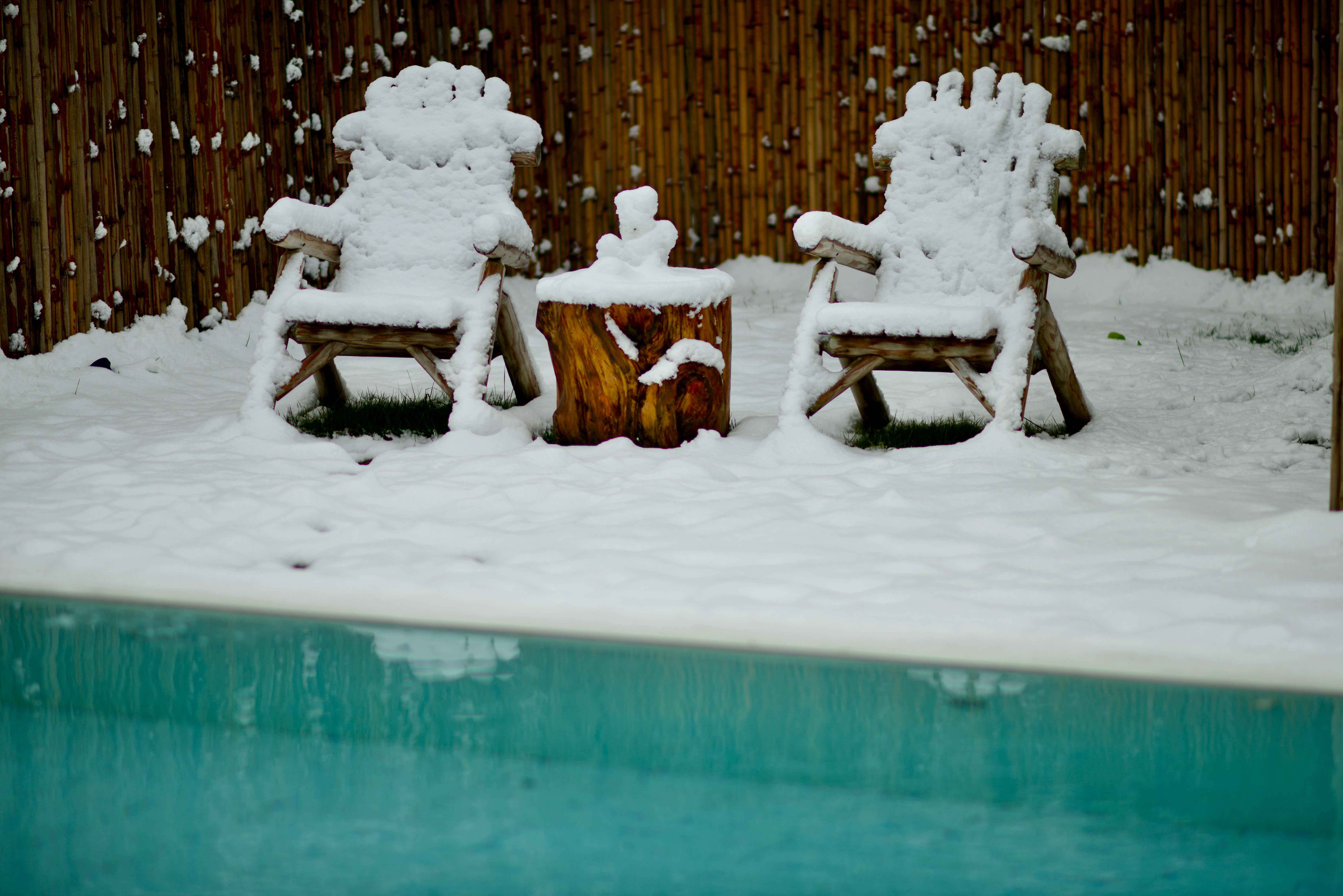 two lawn chairs covered in snow next to a pool