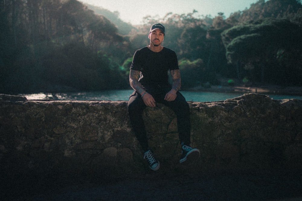 a man sitting on a stone wall next to a river