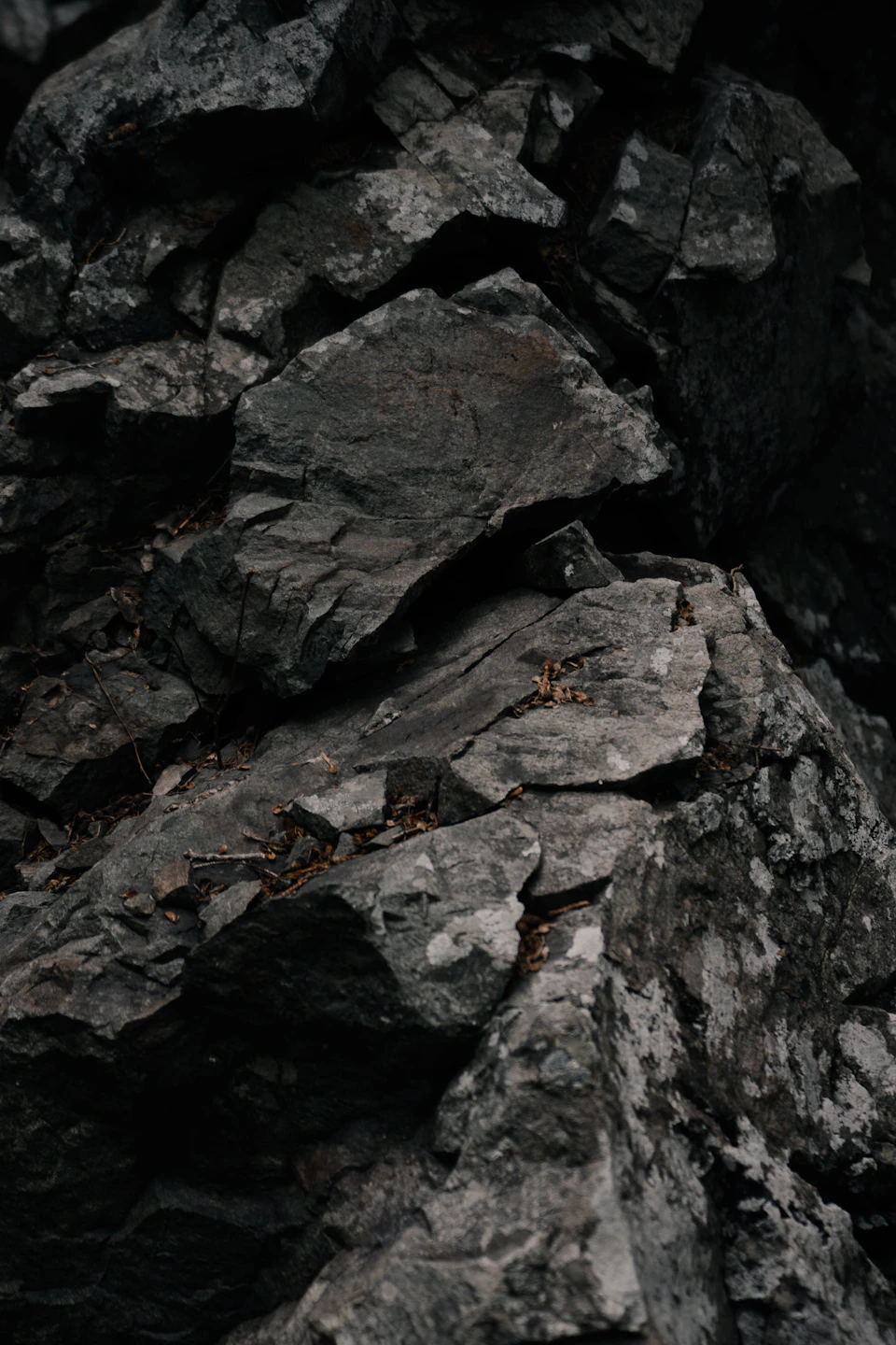 The image shows a close-up view of a large, jagged rock formation composed primarily of gray and black stones. The rocks are arranged in an uneven manner, with some appearing to be cracked or broken. Smaller pieces of moss can be seen on the surface of the rocks, adding a touch of green to the otherwise monochromatic scene.