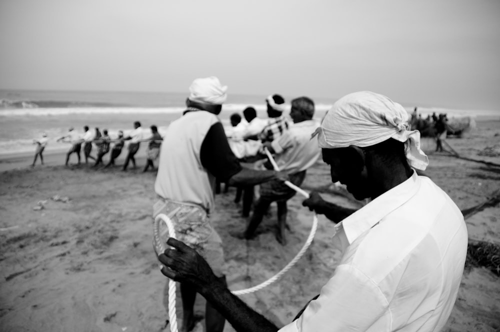 a black and white photo of a man pulling a boat on the beach