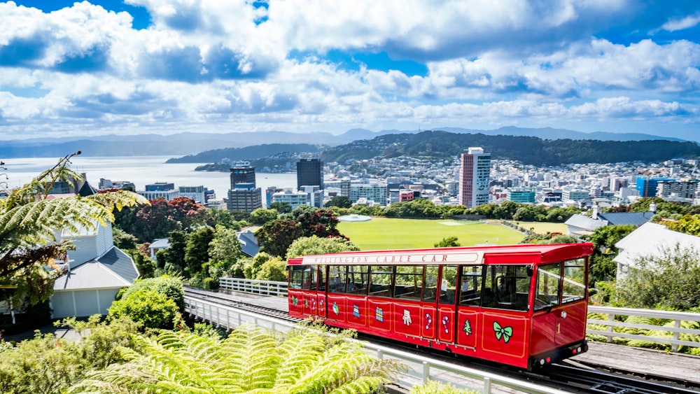 a red trolley on a track with a city in the background