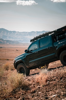 a black truck parked in a field with mountains in the background