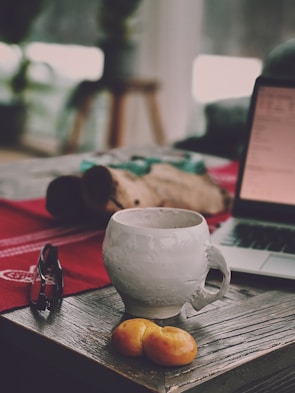 A rustic wooden table with lattidos coffee bags and a steaming cup beside a window.