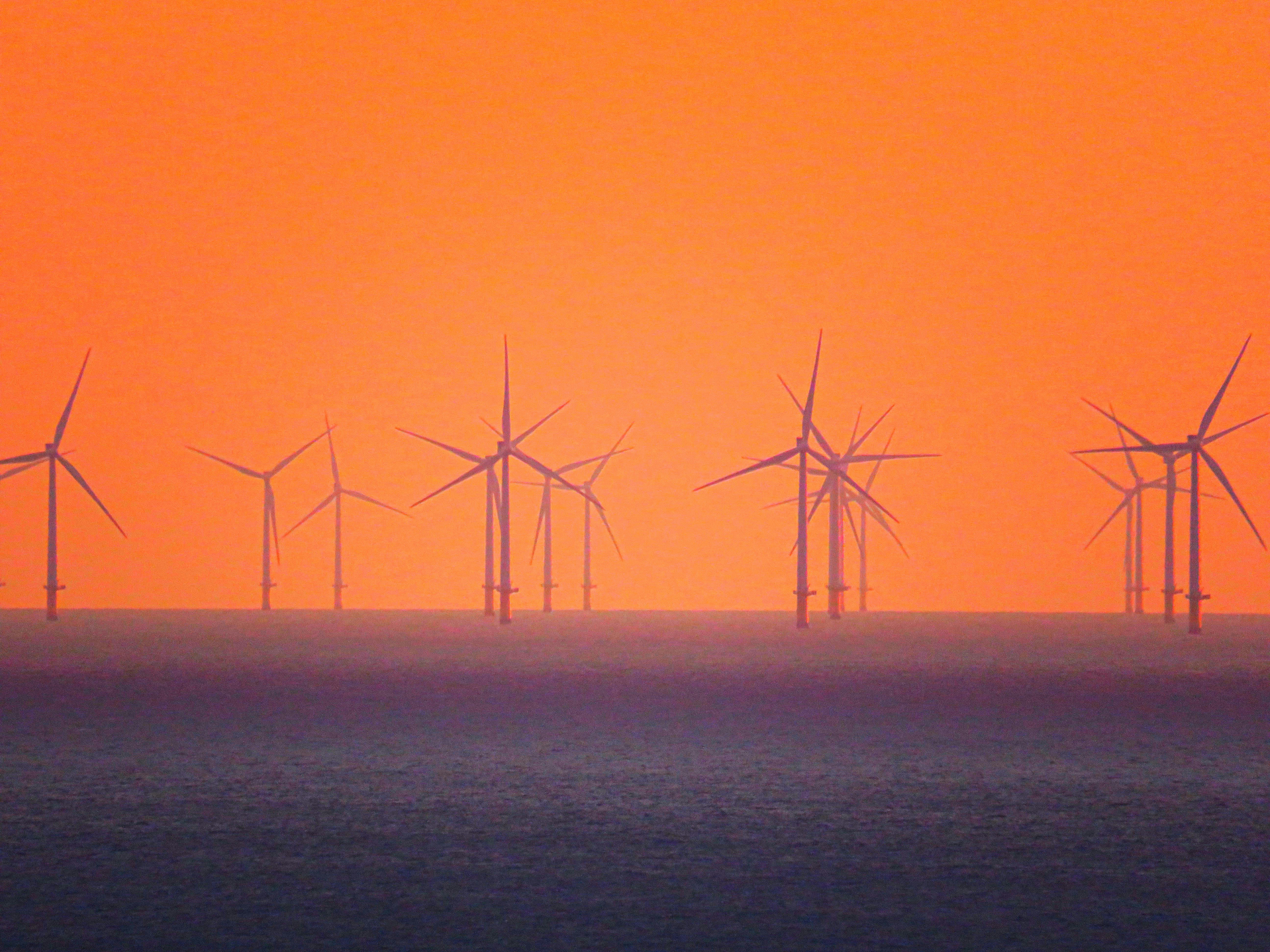 Offshore wind turbines at dusk over calm ocean, dramatic orange sky, industrial scale