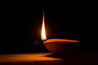 A beautifully lit traditional brass diya with intricate carvings, glowing warmly against a deep purple backdrop.