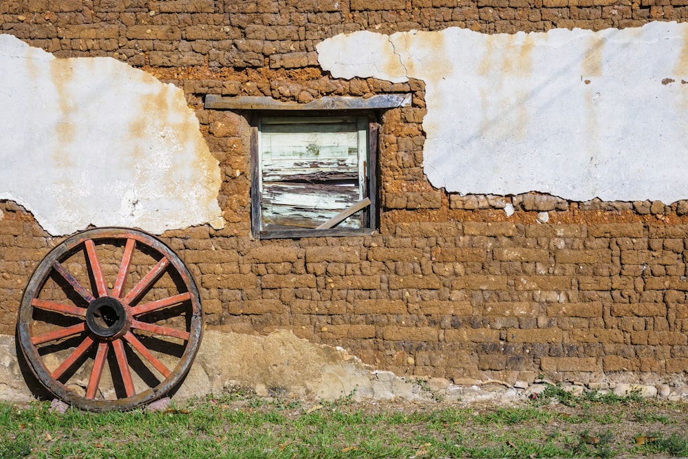 a brick wall with a window and a wagon wheel