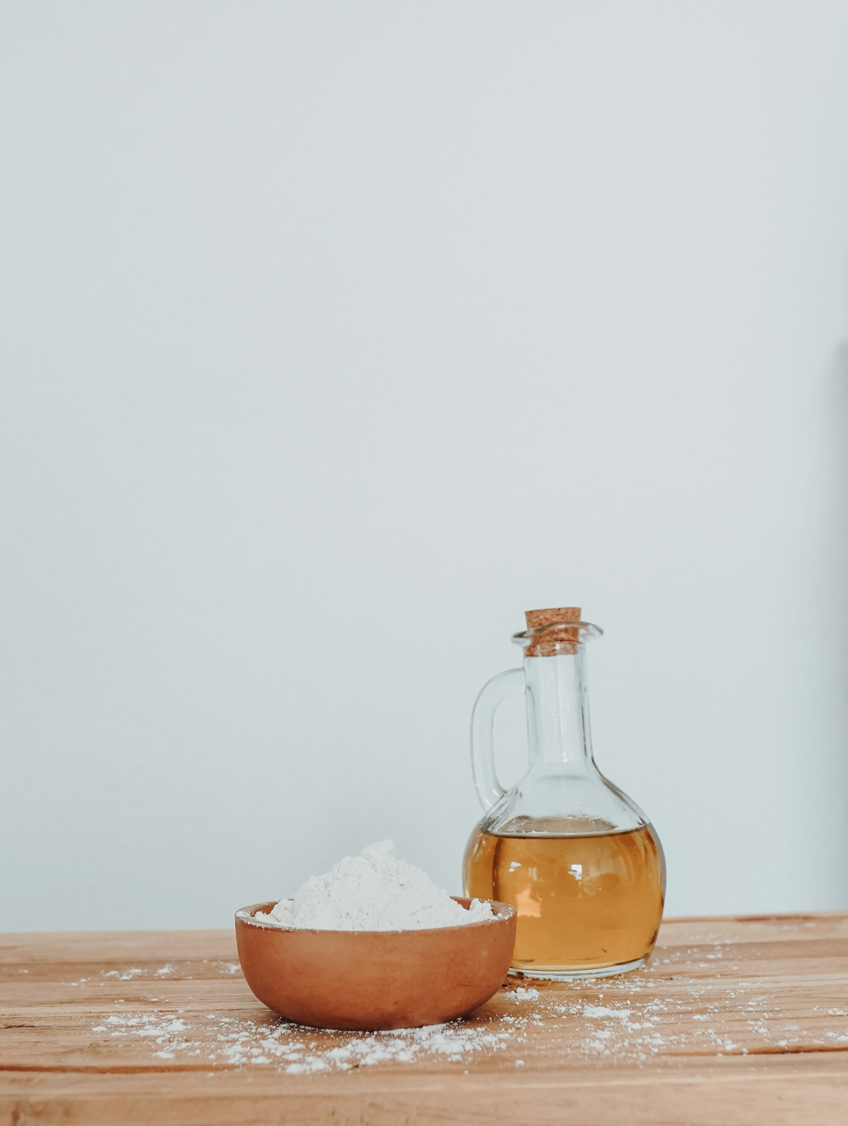 Glaskaraffe mit heller Flüssigkeit neben einer Holzschale mit weissem Pulver auf einem Holztisch