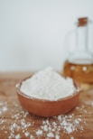 a wooden bowl filled with white powder next to a bottle of honey