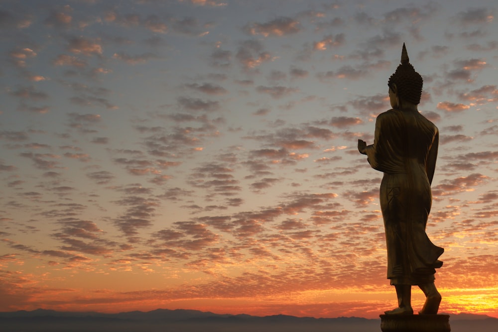 une statue d’une personne debout devant un coucher de soleil
