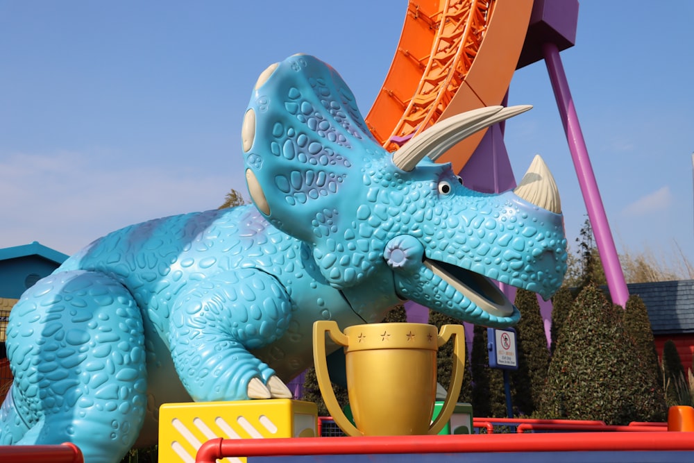 a blue dinosaur statue with a cup in front of it