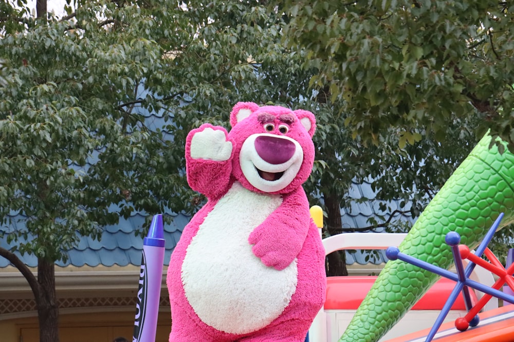 a large pink bear standing next to a giant green leaf