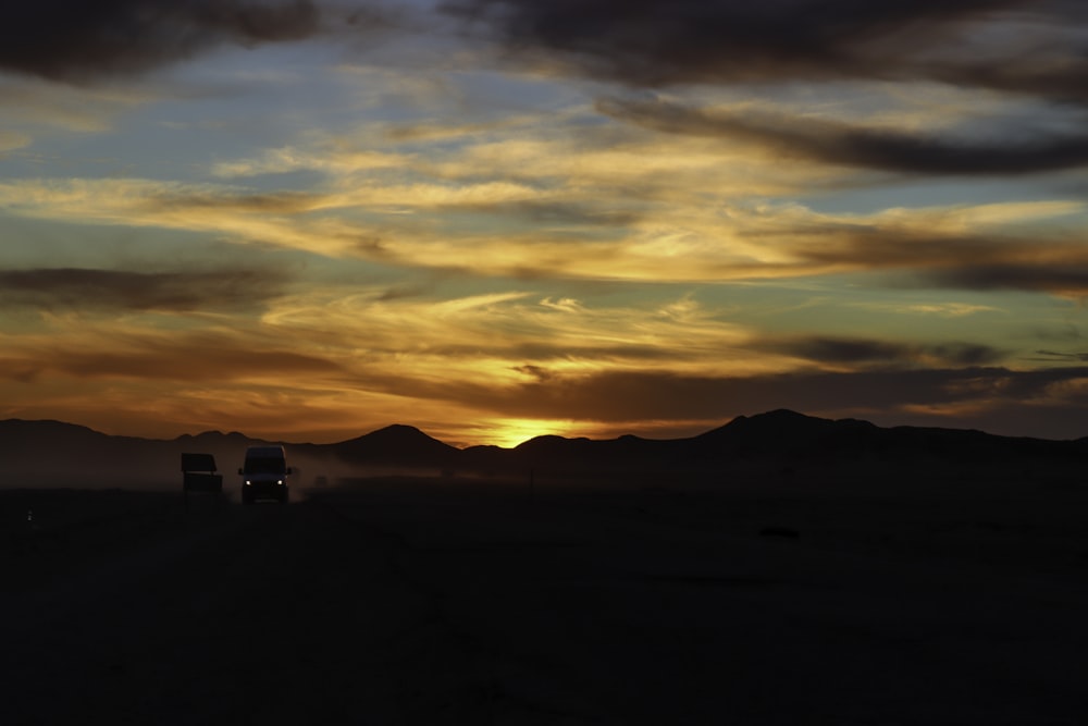 a truck driving down a dirt road under a cloudy sky