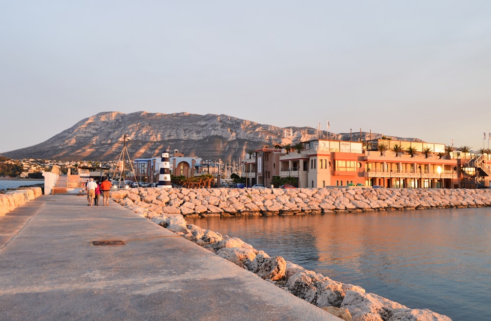 a couple of people walking down a sidewalk next to a body of water