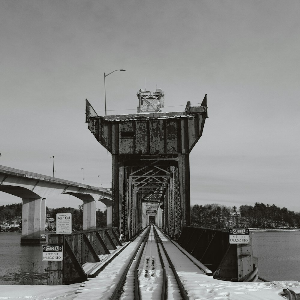 a black and white photo of a train track going under a bridge