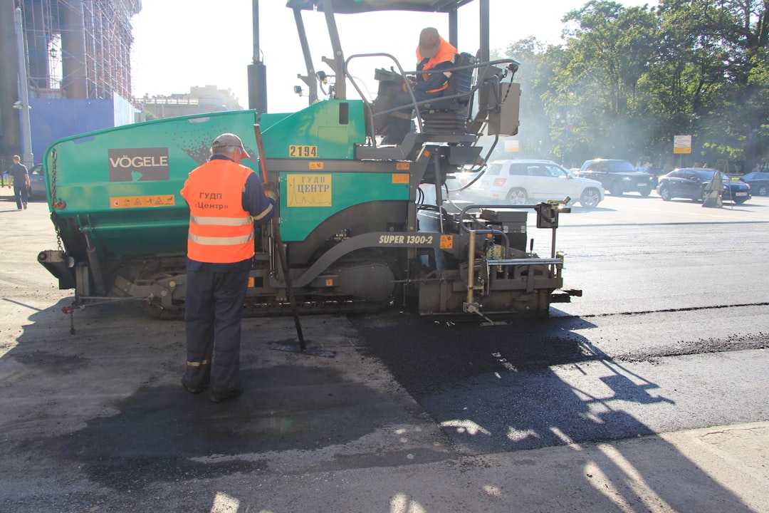 a man standing next to a green and yellow truck, road workers laying asphalt