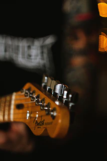 Close-up of a beautifully crafted guitar neck with shiny tuning pegs under warm lighting.