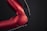 A close-up view of a red metallic robotic arm with visible joints and screws. The arm is connected with black and multicolored wires, set against a dark background, highlighting its mechanical and industrial design.