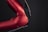 A close-up view of a red metallic robotic arm with visible joints and screws. The arm is connected with black and multicolored wires, set against a dark background, highlighting its mechanical and industrial design.