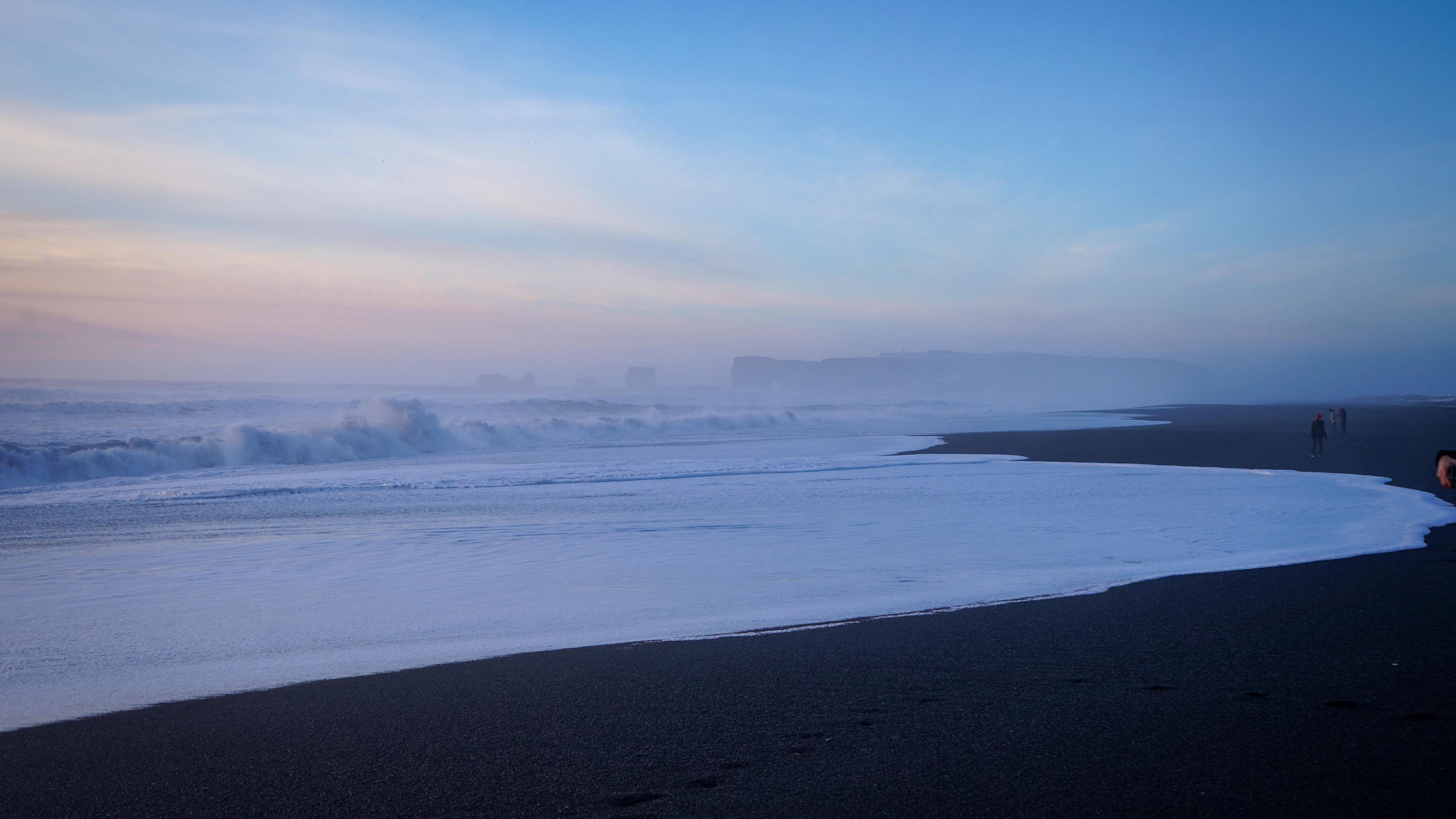 Waves on a black-sand beach on Iceland's south coast in winter twilight, with headlands fading into mist