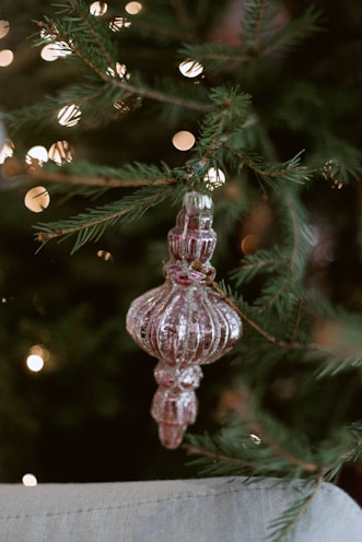 Delicate handmade ornaments hanging on a Christmas tree glowing with warm lights.