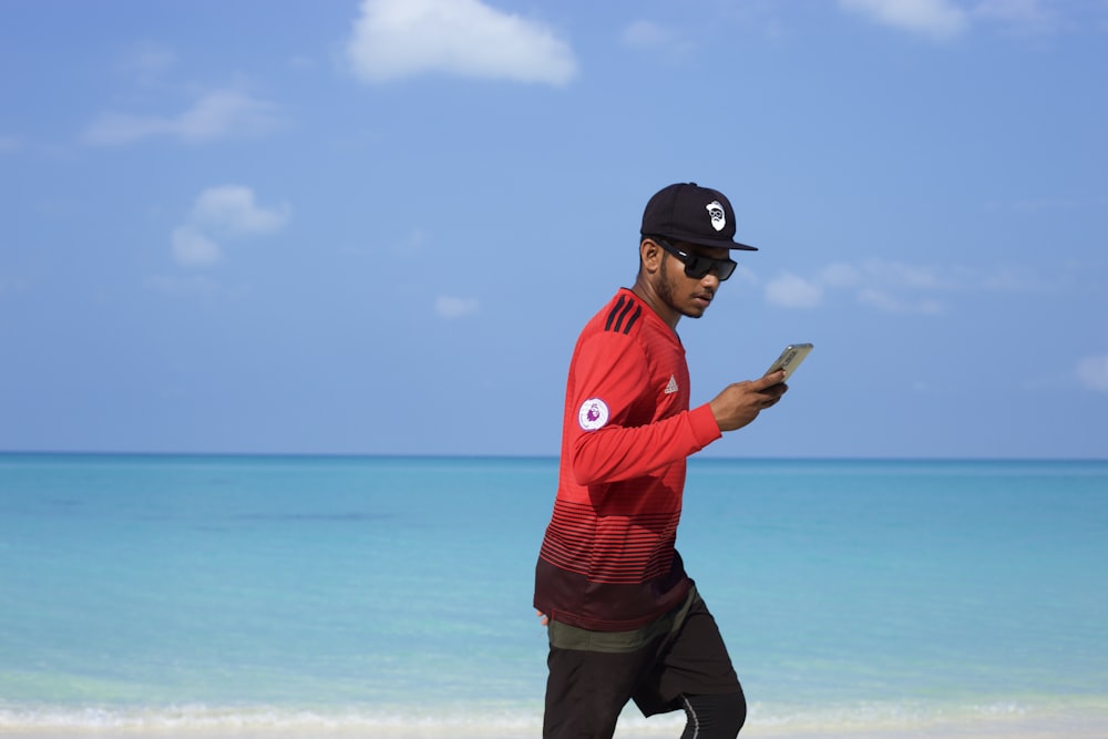a man walking on the beach while looking at his cell phone