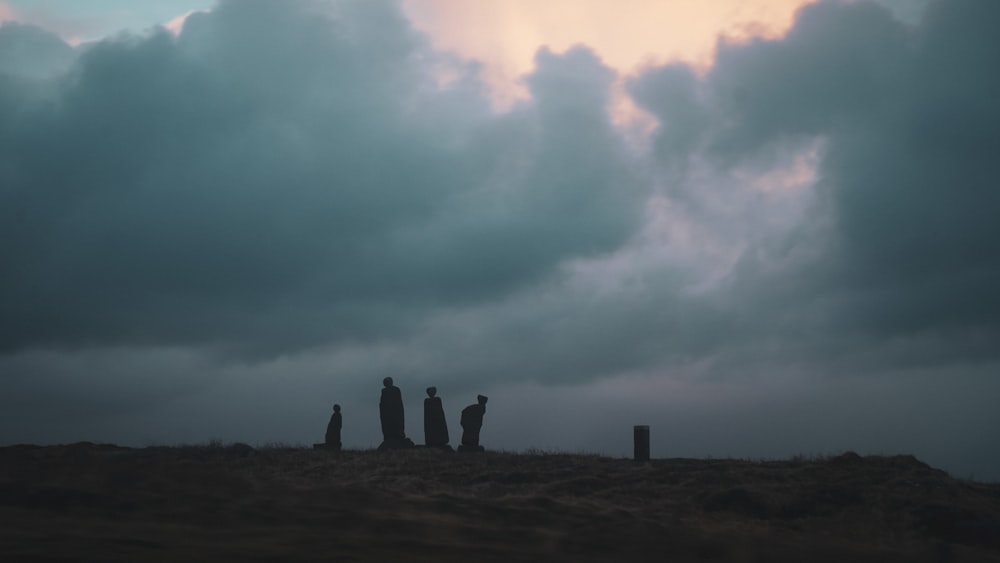 a group of people standing on top of a hill under a cloudy sky