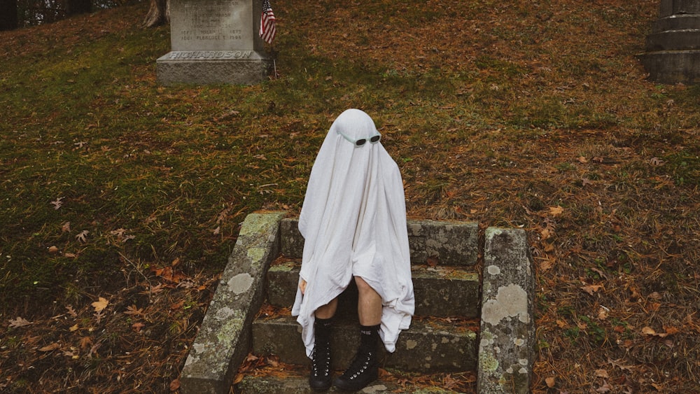 Eine Person in einem Geisterkostüm sitzt auf einem Grab