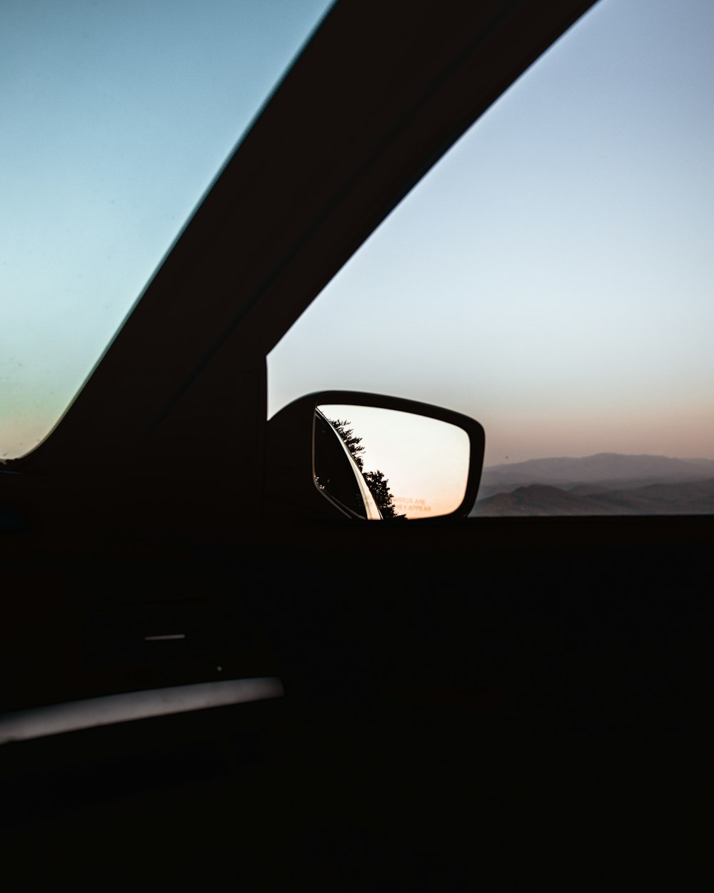 espelho retrovisor lateral de um carro com um pôr do sol no fundo