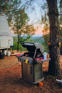 a camper with a grill on the ground next to a tree