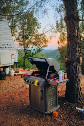 a camper with a grill on the ground next to a tree